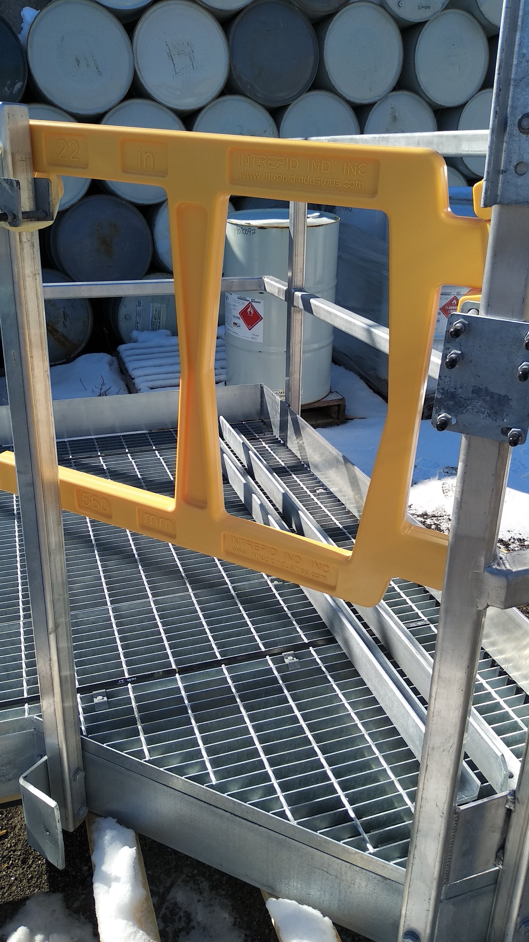 Yellow Intrepid UDG safety gate installed on a galvanized grating platform at an outdoor chemical drum storage area